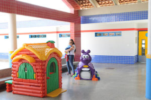 Mulher segura criança pequena no colo em meio a brinquedos coloridos na creche