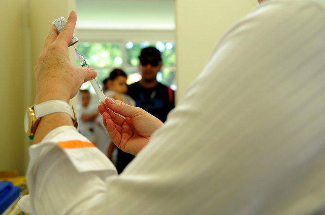 na foto, uma médica segura uma dose da vacina de gripe em uma seringa