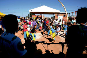 Crianças praticando capoeira ao ar livre e várias pessoas aplaudindo de pé