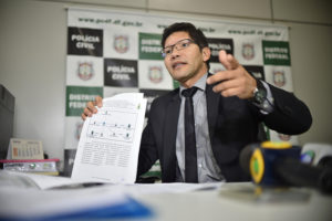 Foto do delegado delegado-chefe responsável pela operação, Alexandre Nicolau Linhares apresentando um documento de investigação