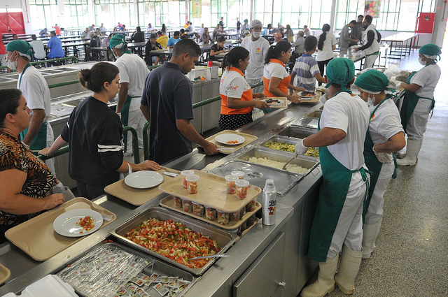 Na foto, pessoas na fila sendo servidas no restaurante comunitário