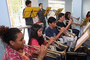 Na imagem algumas crianças aparecem tocando trombone.