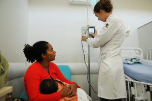 Uma mulher com um bebê em seu colo é atendida por uma médica em um pronto-socorro