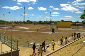  Imagem do Centro Olímpico e Paralímpico de Planaltina. Ao fundo aparecem as quadras de tênis e atletismo. Na imagem também aparecem pessoas caminhando pelo Centro Olímpico. 