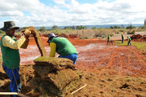 Homens trabalham em terreno colocando grama sintética. 