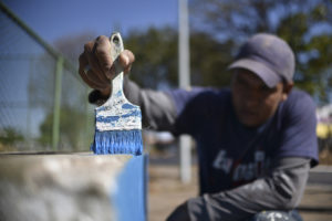 Homem utiliza pincel com tina azul para pintar concreto