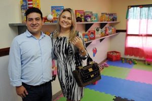 Casal de padrinhos sorri dentro de sala infantil cheia de brinquedos