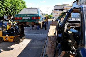 Na imagem, uma carcaça de carro esta sendo retirada da rua.
