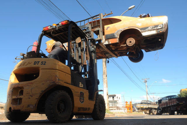 na foto, um trator levanta uma carcaça de um carro velho
