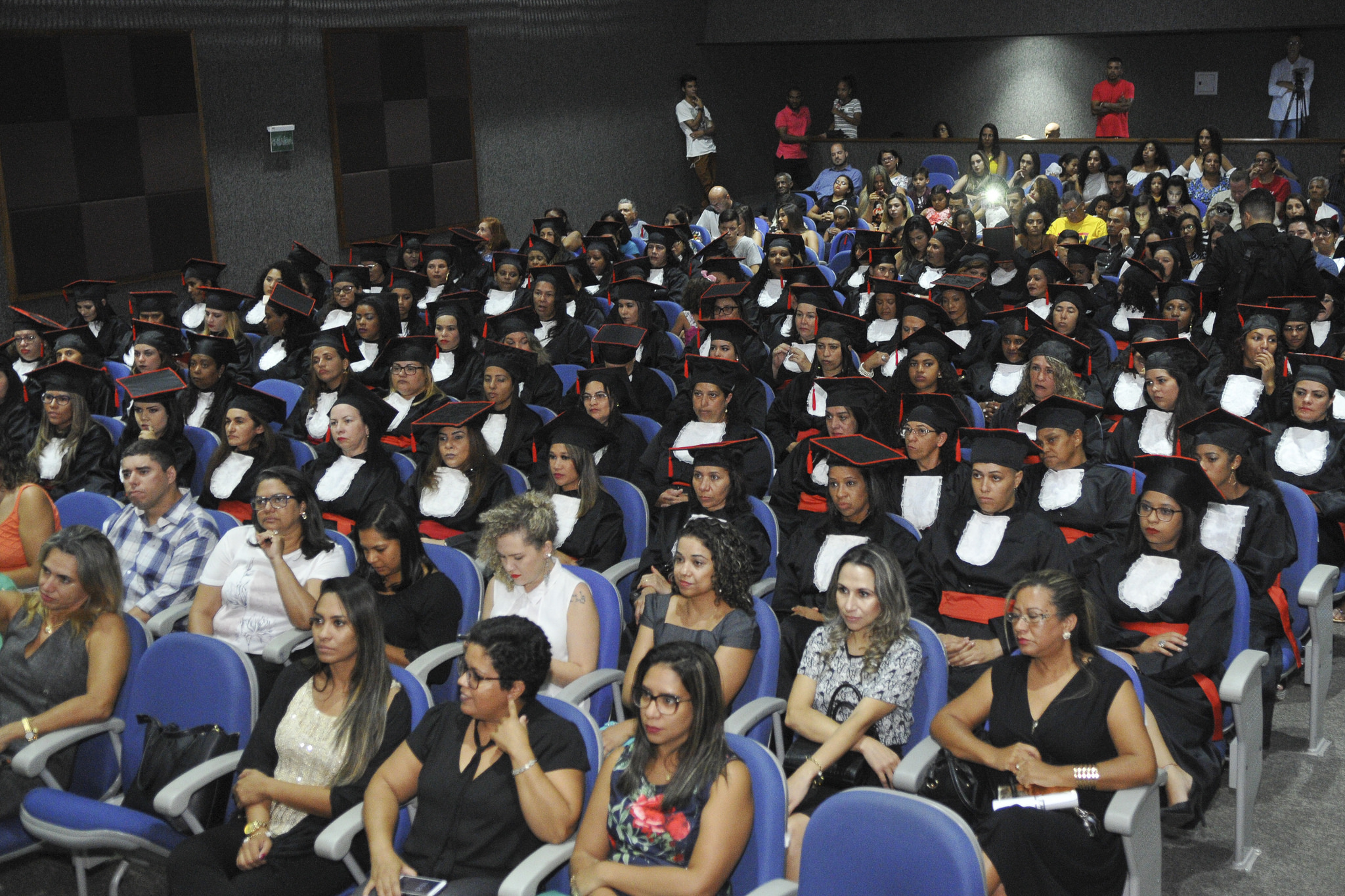mulheres sentadas em um auditório com beca de formatura