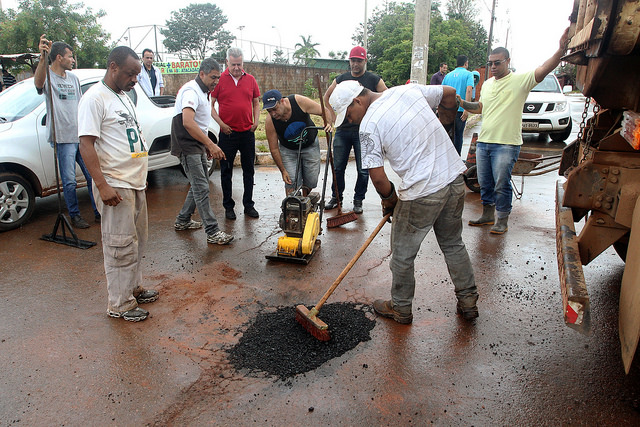 Homens tampam um buraco em uma pista com cimento